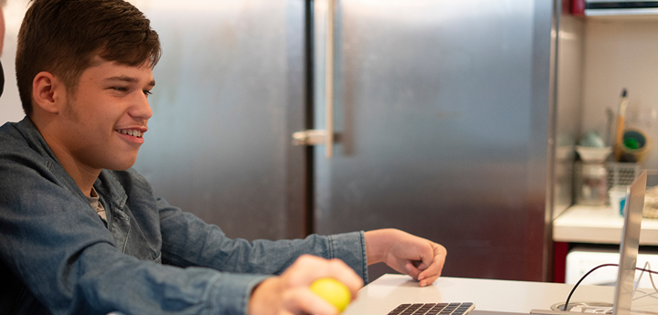 A teenage boy with a disability, sitting in a wheelchair using a laptop