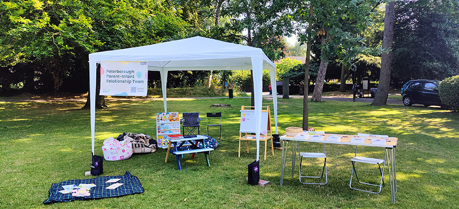 A large area of grass with trees in the background and a gazebo with chairs and tables set out around it.