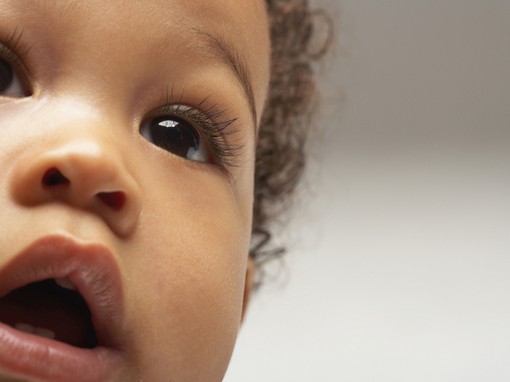 A close-up of a young baby's face staring into the distance with their mouth slightly open