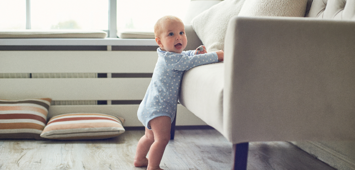 Baby standing up leaning his weight onto a sofa