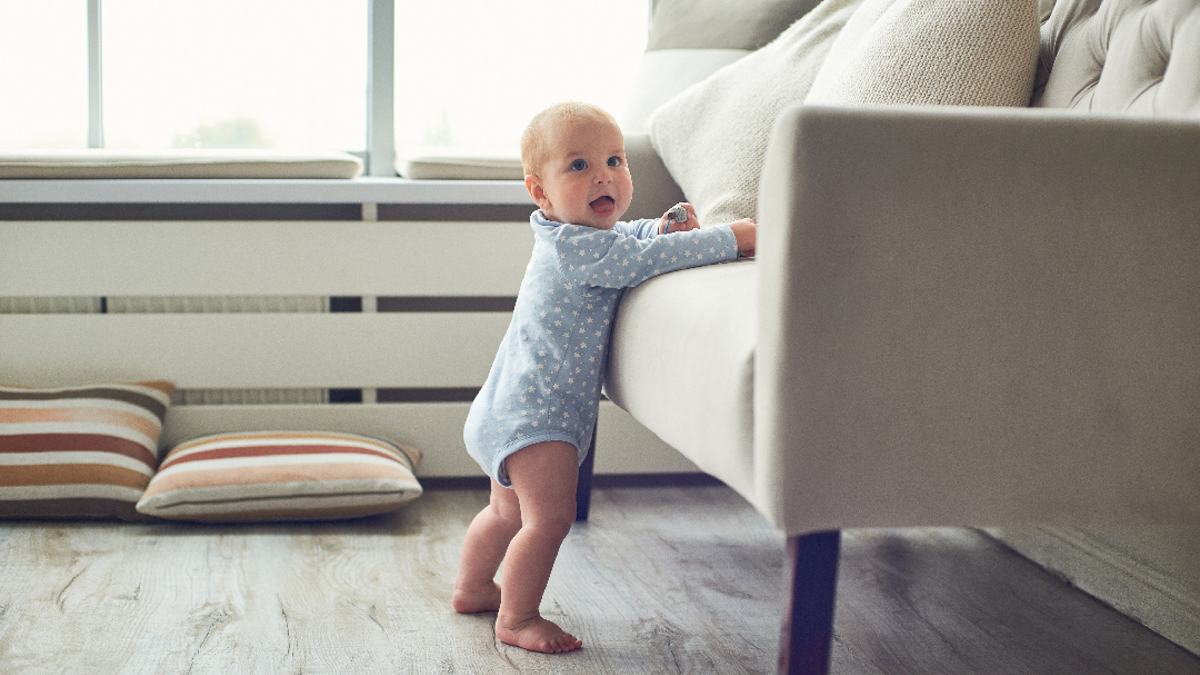 Baby standing up leaning his weight onto a sofa