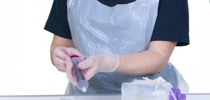 Woman wearing scrubs holding a syringe, with feeding equipment lying on the table in front of her