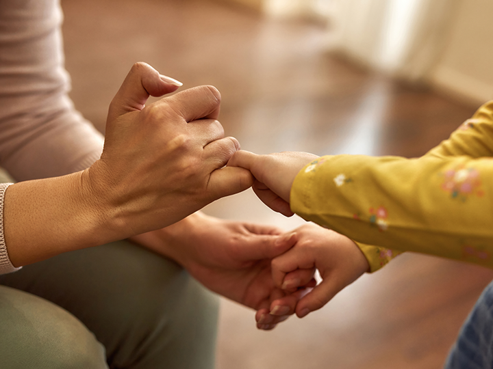 child in yellow long sleeve t-shirt and dungarees holding hands with adult with green trousers and grey jumper