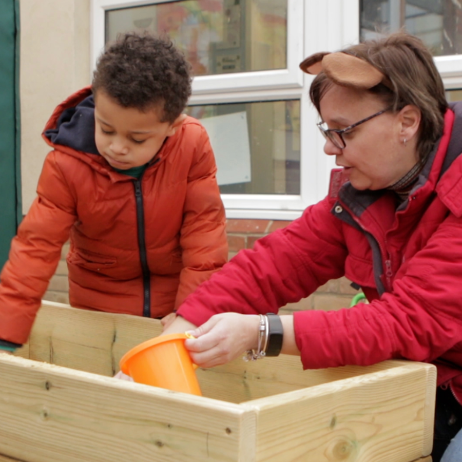 Young boy and teacher playing with a sand pit
